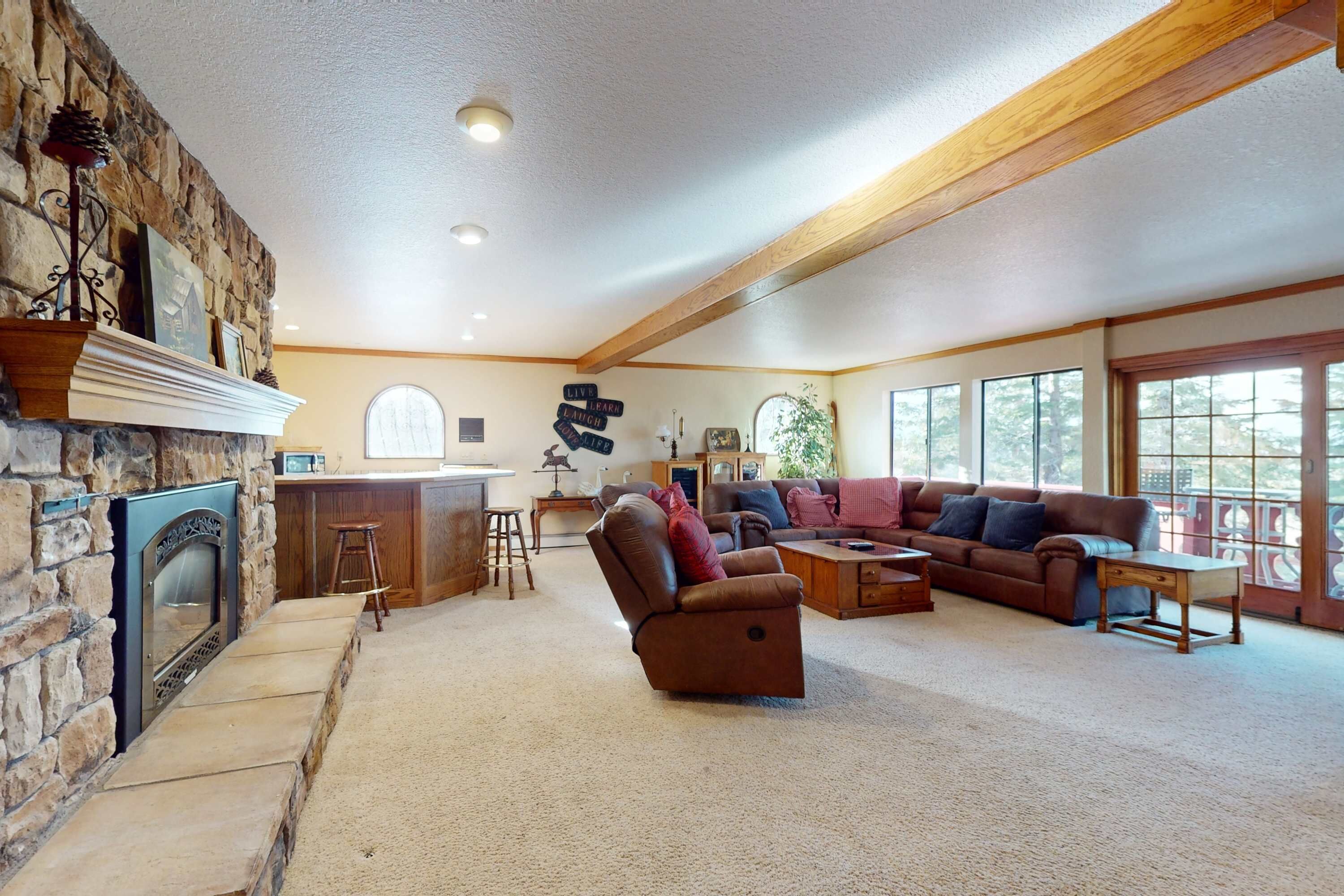 A spacious living room with a stone fireplace, a leather recliner, a sofa, and a dining area with a bar.