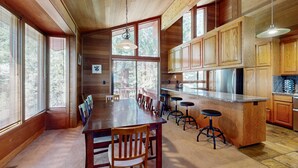 Un interior de madera con una mesa de comedor, taburetes de bar y ventanas amplias.