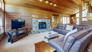 Una sala de estar con chimenea de piedra, techo de madera, sofá de cuero y televisor.