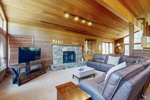 Ein Wohnzimmer mit Kamin aus Stein, Holzbalkendecke, Ledersofa und Fernseher.