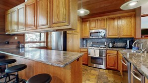 Una cocina con armarios de madera, electrodomésticos de acero inoxidable, encimera de granito y taburetes de bar.