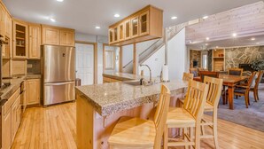 Una cocina moderna con armarios de madera, un refrigerador de acero inoxidable, encimeras de granito y un comedor con sillas y mesa de madera.