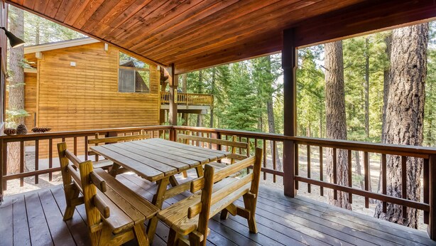 Una terraza de madera con una mesa y bancos, con vistas a una zona boscosa.