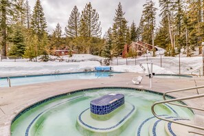 A pool with a blue tiled hot tub surrounded by snow-covered ground and trees.