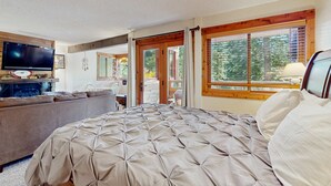 Un dormitorio con una cama grande, televisión, sofá y vistas al exterior a través de las ventanas.