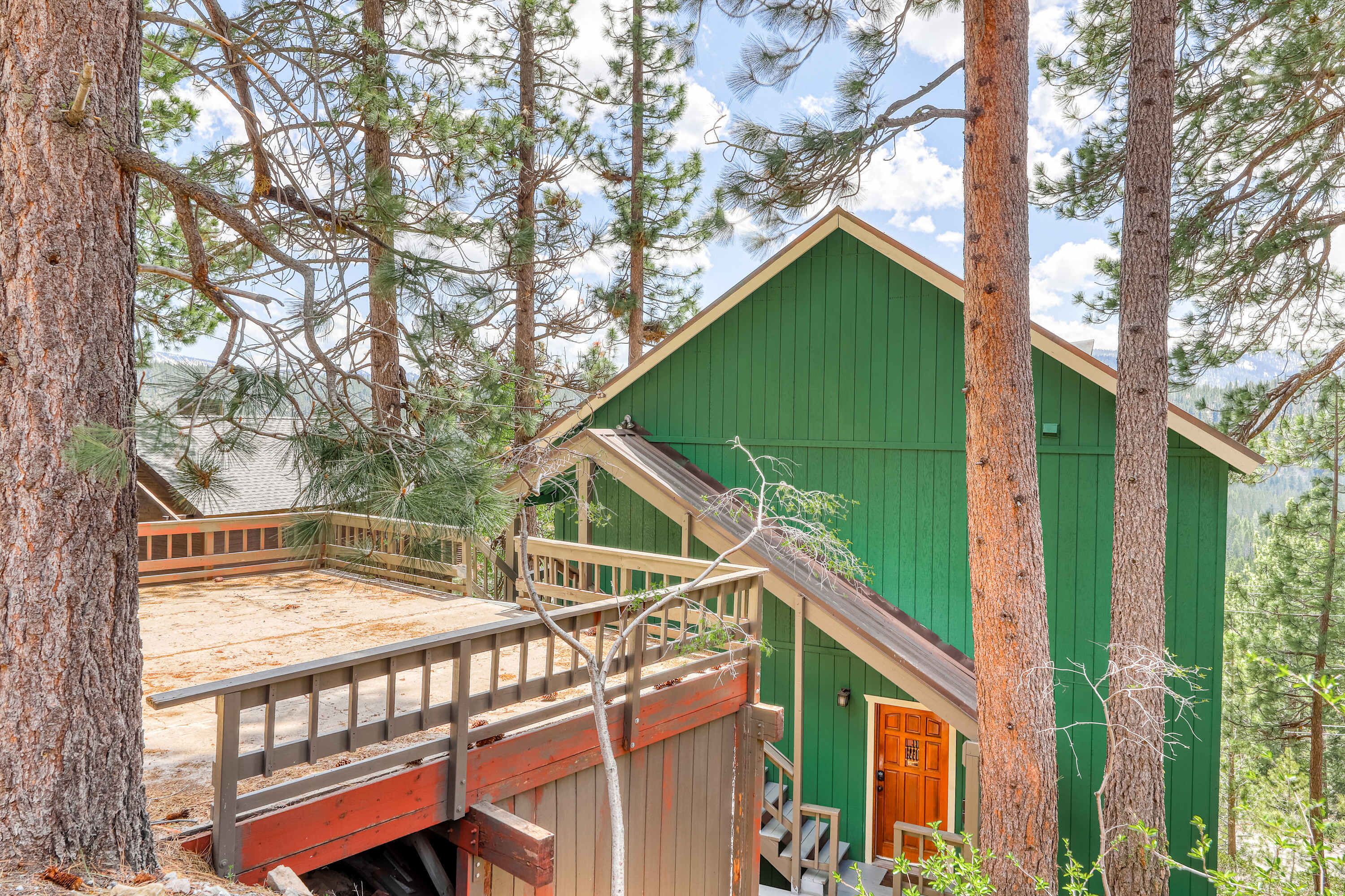 A cabin with a wooden deck, a green exterior, and a staircase leading to the main entrance.