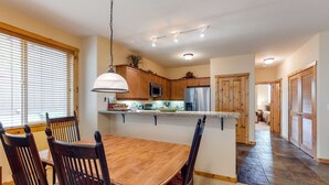A dining area with a wooden table and chairs, a kitchen with wooden cabinets and appliances, and a hallway with wooden doors. - Quiet mountain home w/private deck/gas grill/shared pool - near lakes (Truckee)