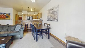 Una sala de estar con un sofá, una mesa de comedor con sillas, una cocina al fondo y un cuadro en la pared.