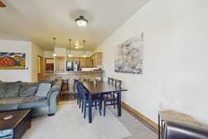 A living room with a sofa, a dining table with chairs, a kitchen in the background, and a painting on the wall. - Beautiful condo w/ deck, close to town & skiing (Truckee)