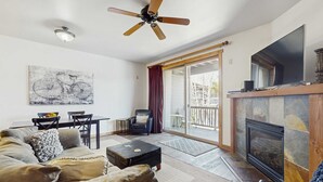 Una sala de estar con sofá, mesa de centro, chimenea, ventilador de techo y comedor con sillas y mesa.