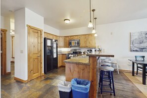 A modern kitchen with wooden cabinets, a black refrigerator, a microwave, and a granite countertop island. - Beautiful condo w/ deck, close to town & skiing (Truckee)