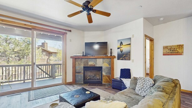 Una sala de estar con chimenea, ventilador de techo, televisor grande y puerta corrediza de vidrio a una terraza.