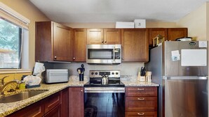 Una cocina funcional con gabinetes de madera, microondas de acero inoxidable, horno y refrigerador.