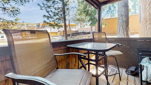 Un área de estar techada al aire libre con sillas y una mesa, con vista a un estacionamiento y edificios.