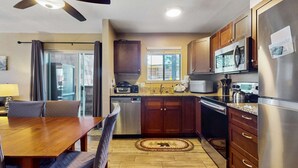 Una cocina moderna con armarios de madera, electrodomésticos de acero inoxidable, un comedor con mesa y sillas de madera, y un ventilador de techo.