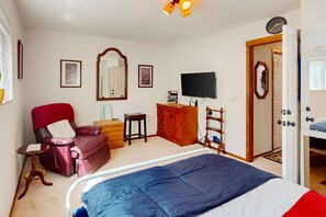 Ein Schlafzimmer mit einem Bett, einem roten Ledersessel, einer Holzkommode, einem Fernseher und einer Tür zu einem anderen Raum.