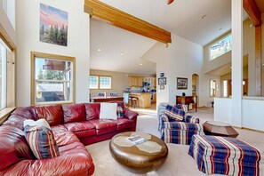 A spacious living area with a red leather sofa, striped ottoman, and a wooden coffee table. - Serene home with mountain views, deck, fireplace, BBQ, (Truckee)