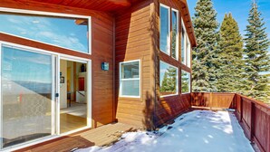 Una cabaña de madera con ventanas grandes, una terraza y vistas a árboles nevados.