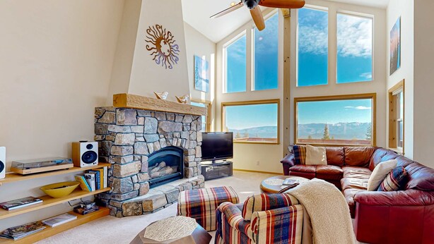 Un salón amplio con chimenea de piedra, sofá de cuero y ventanas grandes con vistas.