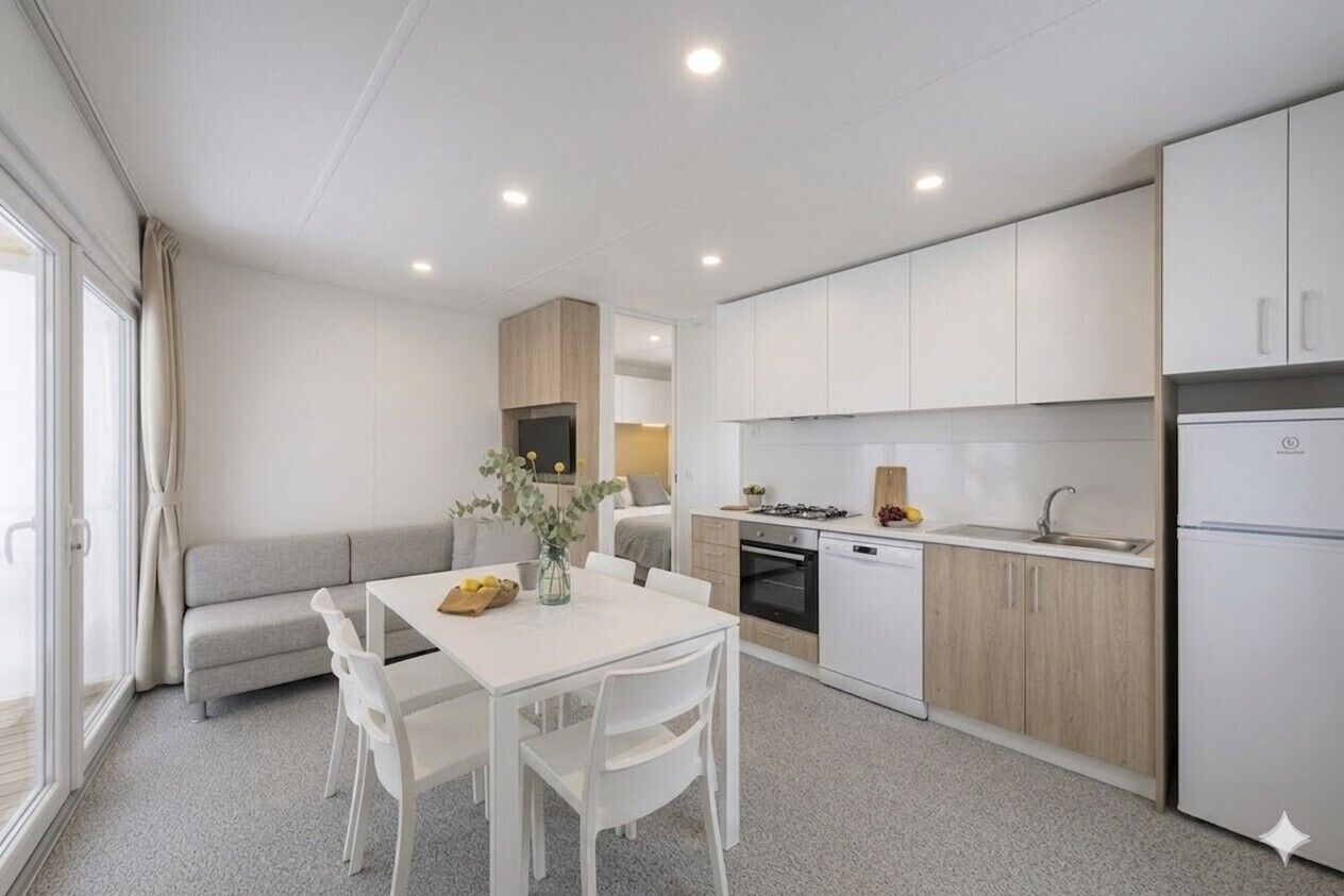 A modern kitchen with white cabinetry, a dining area with a white table and chairs, and a grey sofa.