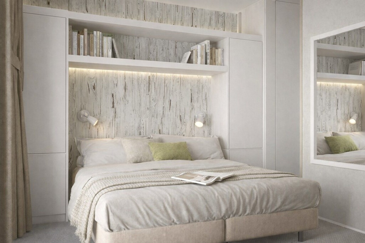 A modern bedroom with a bed, built-in shelves, a mirror, and a wall-mounted light fixture.