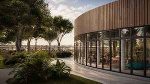 A modern building with a curved wooden facade, large glass windows, and a landscaped outdoor area with trees and seating. - Delta Open Air Resort (Porto Garibaldi)