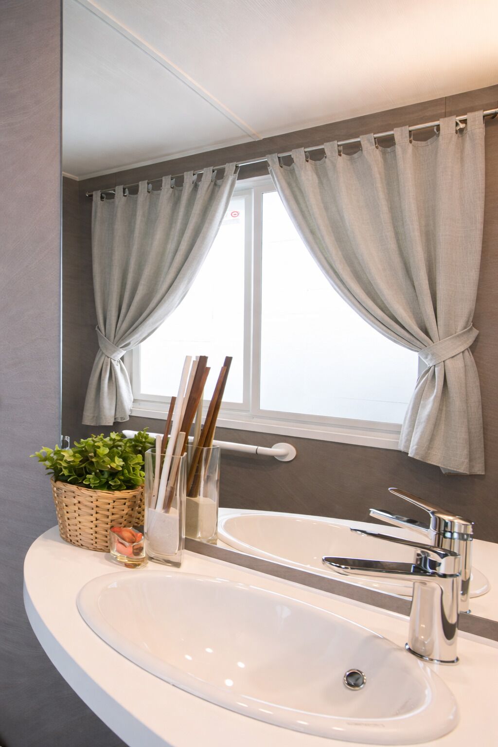 A bathroom with a white sink, a mirror, and a window with curtains.