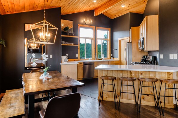 Een moderne keuken met houten kastjes, een centraal eiland met krukken, een kroonluchter en grote ramen.