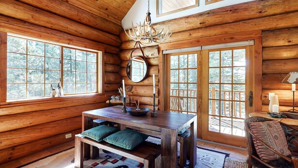 A log cabin interior with a wooden dining table, benches, a chandelier, and large windows. - Dog-Friendly Classic Log Cabin with Game Room, Deck & Views (Truckee)