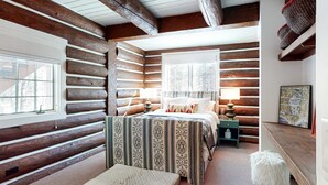 A log cabin bedroom with a bed, two bedside tables, a window, and a fireplace. - Dog-Friendly Classic Log Cabin with Game Room, Deck & Views (Truckee)