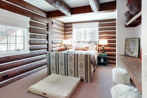 A log cabin bedroom with a bed, two bedside tables, a window, and a fireplace. - Dog-Friendly Classic Log Cabin with Game Room, Deck & Views (Truckee)