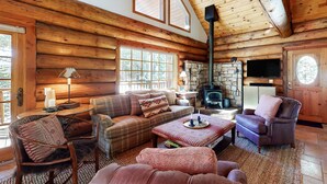 A log cabin interior with a fireplace, wooden walls, a sofa, a chair, and a dining table. - Dog-Friendly Classic Log Cabin with Game Room, Deck & Views (Truckee)