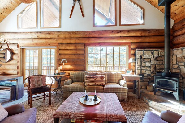 L’intérieur d’une cabane en rondins, avec une cheminée en pierre, des meubles en bois et de grandes fenêtres.