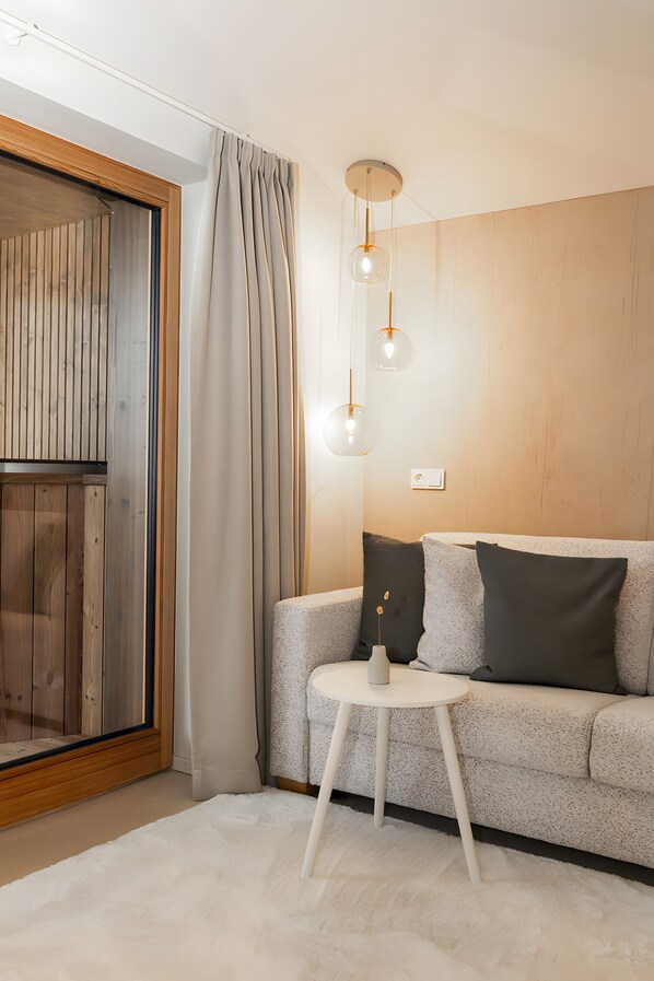 A modern living room with a wooden floor, a grey sofa with cushions, a small white table, and a hanging light fixture.