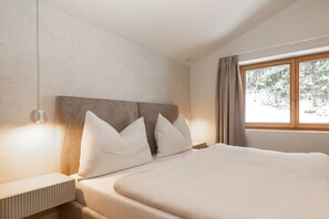 A bedroom with a large bed, a headboard, bedside lamps, and a window with curtains. - Apartment “N°1” with Mountain View, Private Terrace and Wi-Fi (Hüttschlag)