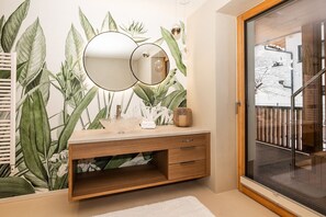 Een badkamer met een houten wastafelmeubel, een grote spiegel en een muur met een tropische plantenmuur.