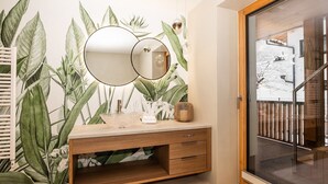 A bathroom with a wooden vanity, a large mirror, and a wall with a tropical plant mural.