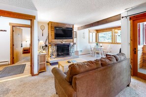 A living room with a fireplace, television, and a sofa. - Second-Level Condo with Free WiFi, Wood Fireplace, Shared Outdoor Pool, & Views (Tahoe City)