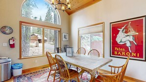 A dining area with a wooden table, chairs, large windows, and a chandelier. - Spacious & Sunny Tahoe Donner Home - Enjoy Access to 5-Star Amenities (Truckee)