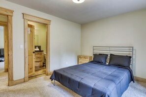 Une chambre à coucher avec un lit, une table de chevet, une armoire en bois et une salle de bain visible à travers une porte ouverte.