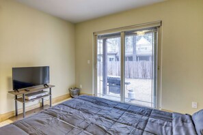 Une chambre à coucher avec un lit, un téléviseur posé sur un meuble et une porte-fenêtre coulissante donnant sur un jardin.