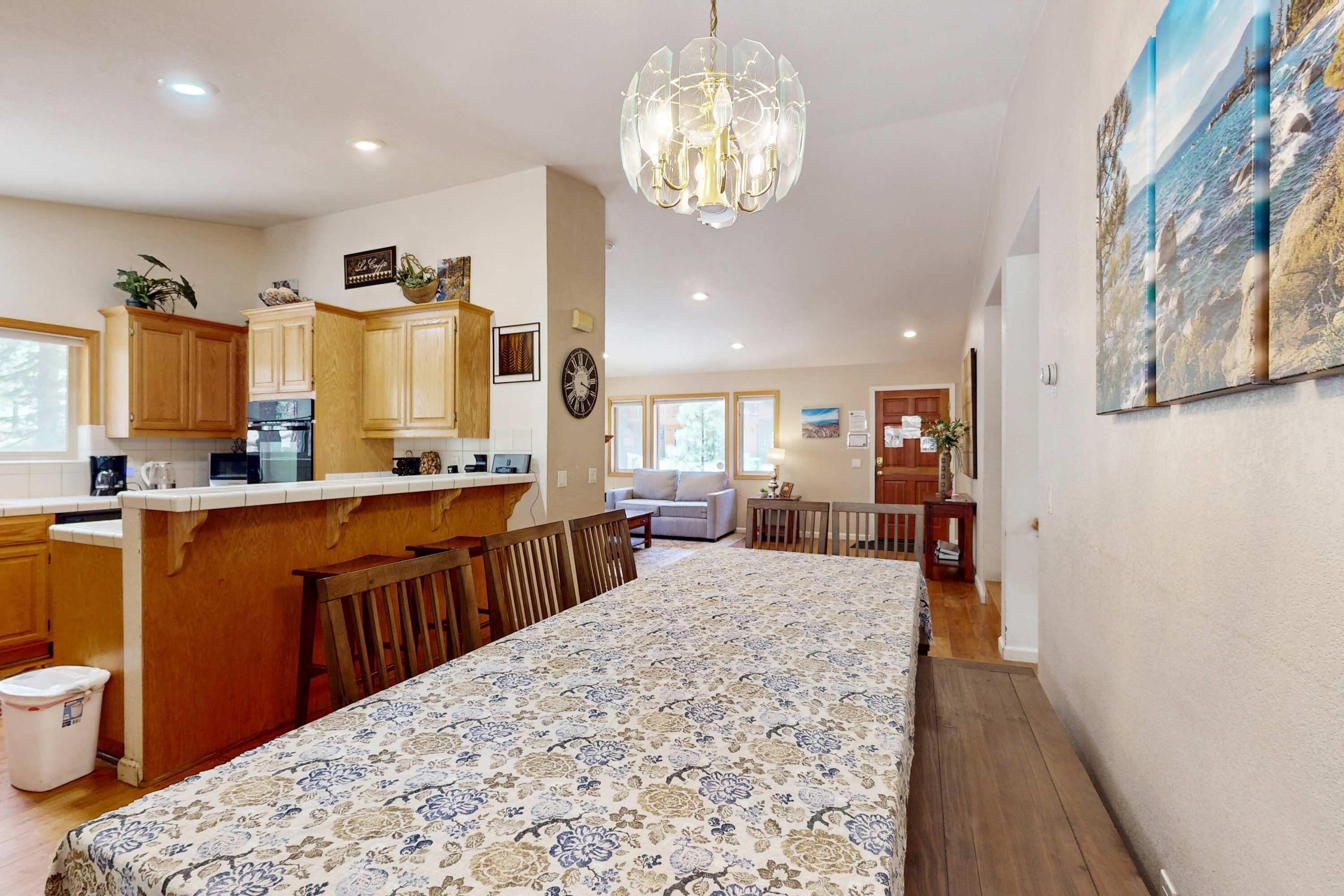 A spacious kitchen with wooden cabinets, a dining area with a patterned tablecloth, and a large window.