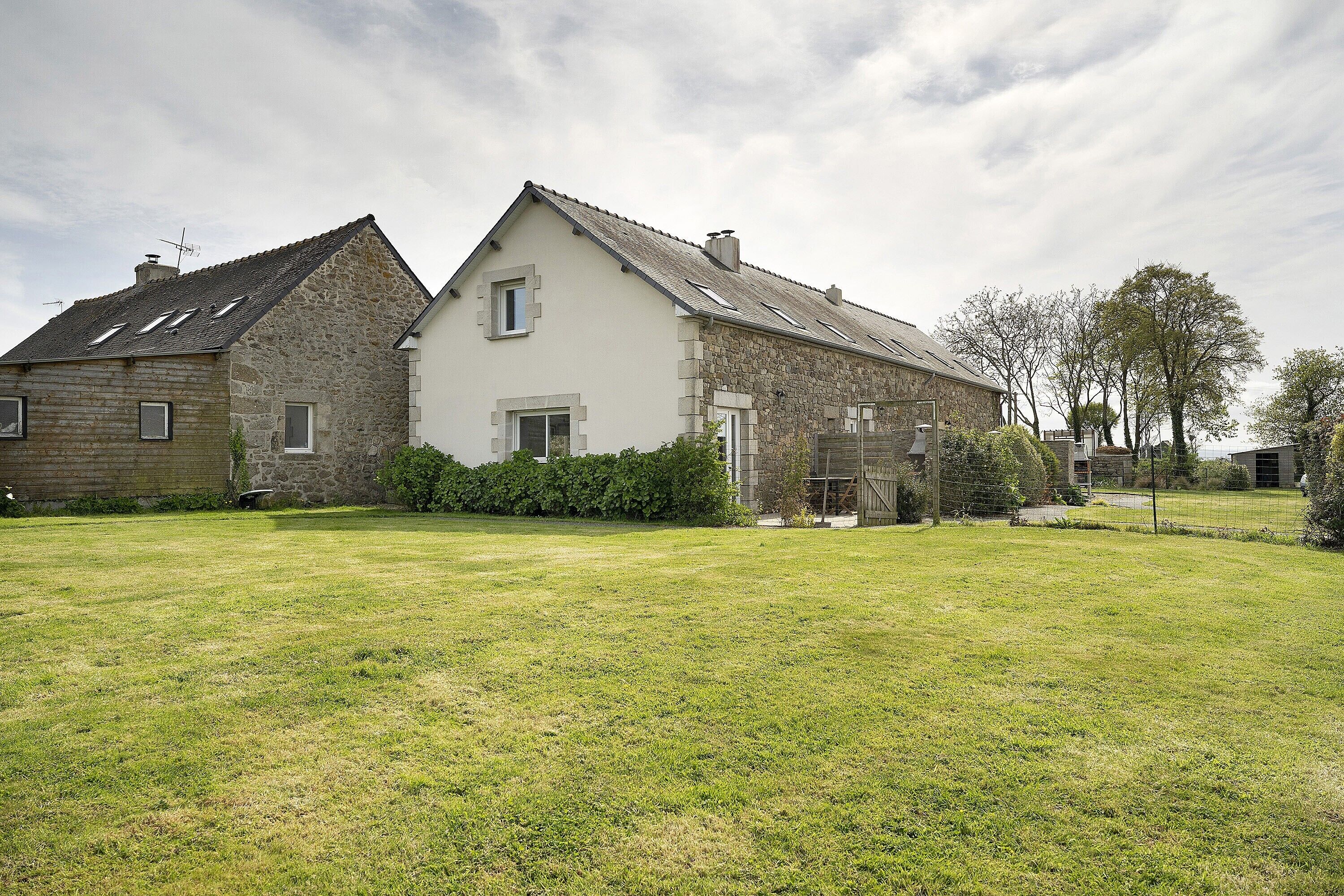 A stone house with a sloped roof, a grassy yard, and a hedge.
