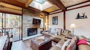 Una sala de estar acogedora con chimenea de piedra, sofás de cuero, techo de madera con tragaluces y una pared de piedra.