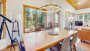 Un comedor con una mesa de madera, sillas, una lámpara y un ventanal con vistas a árboles.