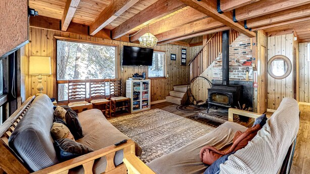 En mysig stuga med träpanel i taket, en öppen spis, en tv och en soffa.