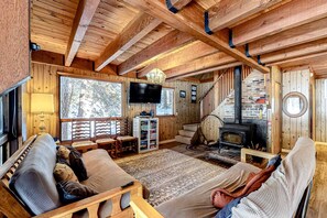 Ein gemütliches Blockhaus-Interieur mit Holzbalkendecke, Kamin, Fernseher und einer Couch.