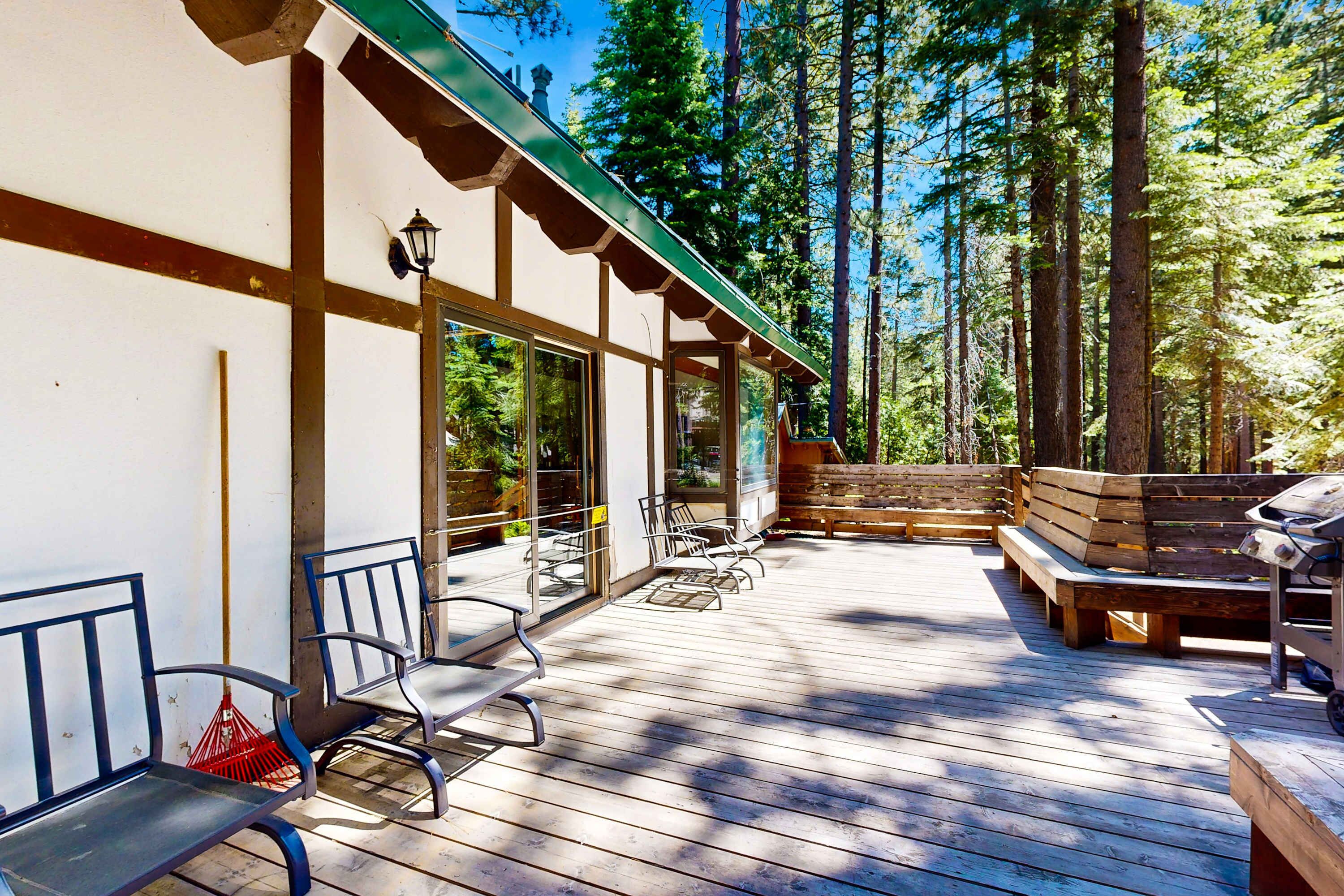 A wooden deck with benches and a grill, surrounded by tall trees.