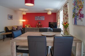 Ein modernes Wohnzimmer mit roter Akzentwand, einem Esstisch mit Stühlen, einer Couch, einem Fernseher und einem blumigen Vorhang.