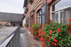 Un bâtiment en briques doté d’un balcon, orné de fleurs rouges et entouré d’une clôture en métal.